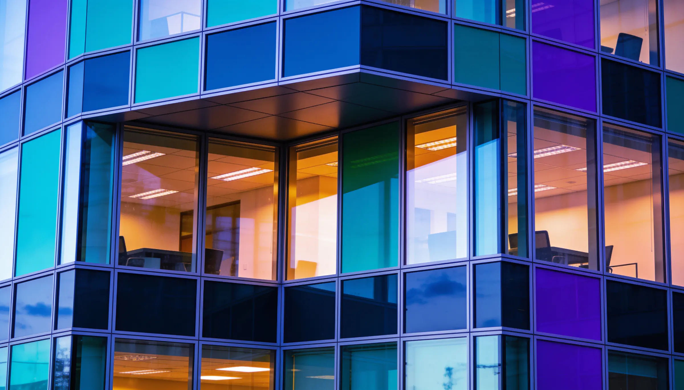 Lit offices behind the green and violet glass facade of a corporate building